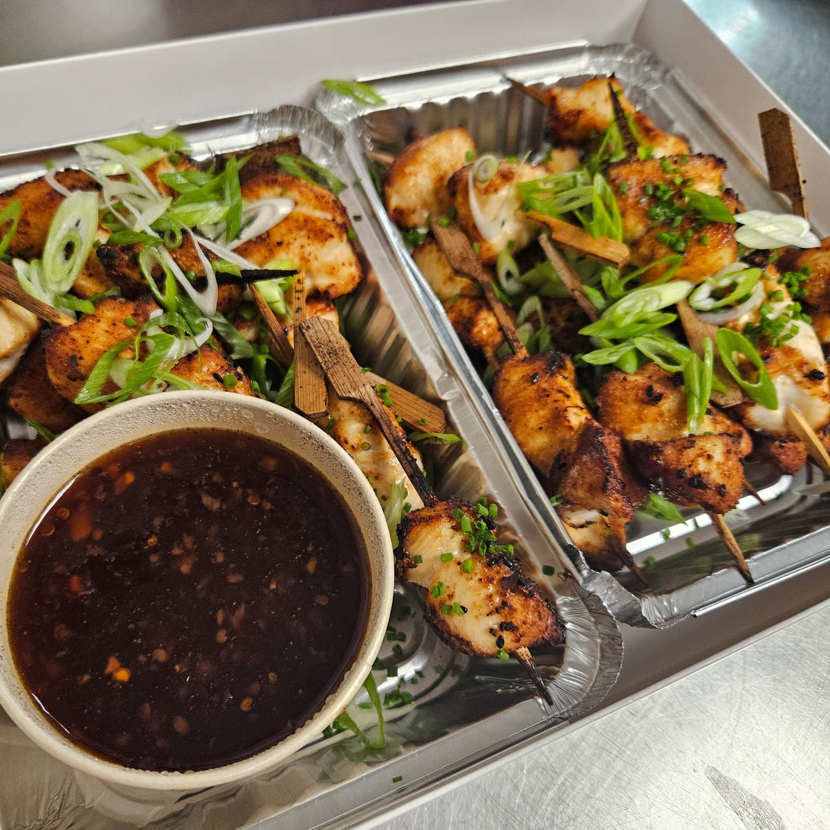 Catering tray of sweet and spicy Thai chicken skewers on bamboo picks, garnished with green onion and toasted sesame, with dipping sauce — Radical Gardens, Timmins