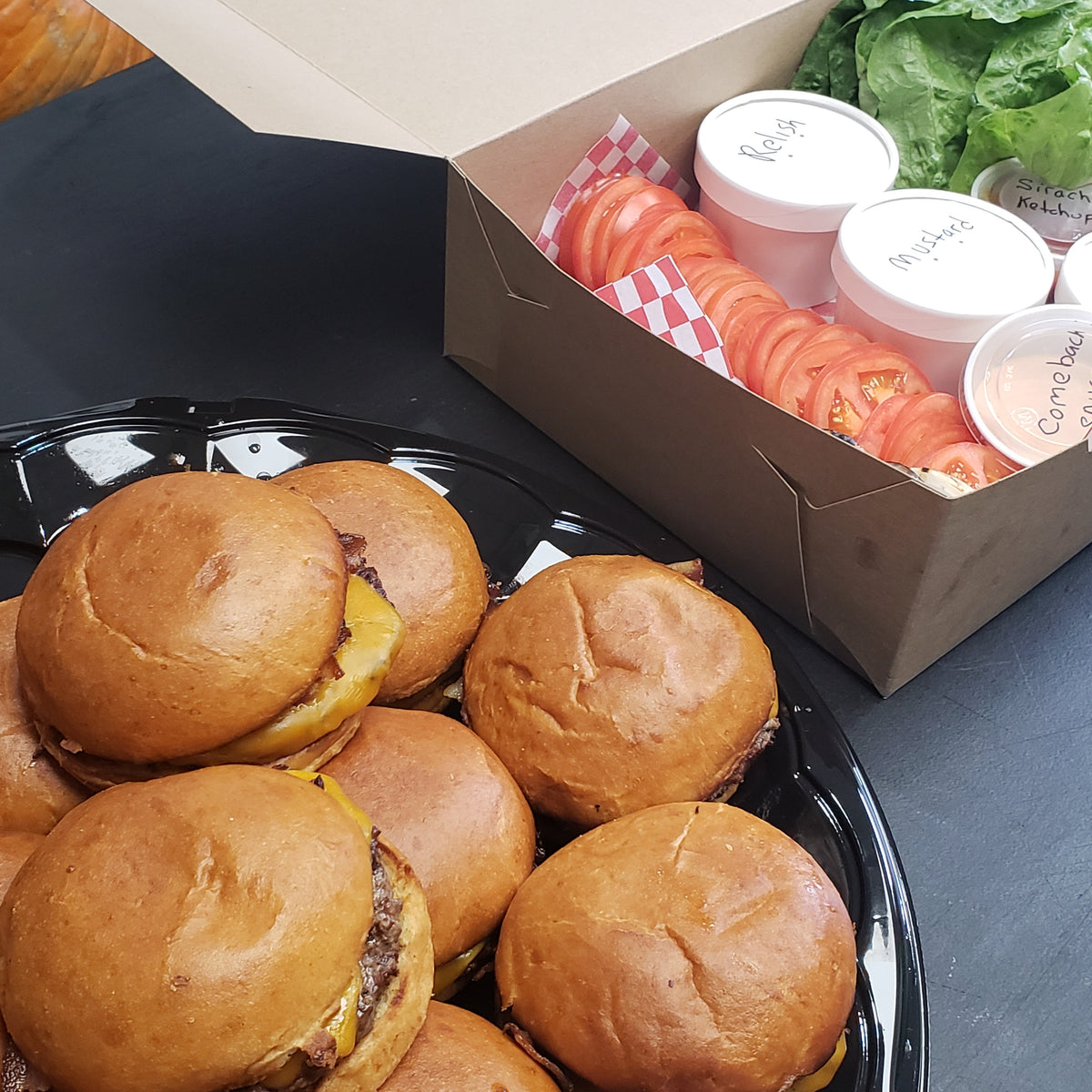 A set of burger patties with toppings and condiments on a table, for catering or event purposes.
