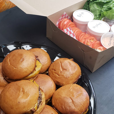 A set of burger patties with toppings and condiments on a table, for catering or event purposes.