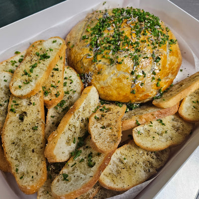 A whole brie wheel wrapped in puff pastry with a scored design on top, baked until gooey, served with crostini for dipping — Radical Gardens, Timmins